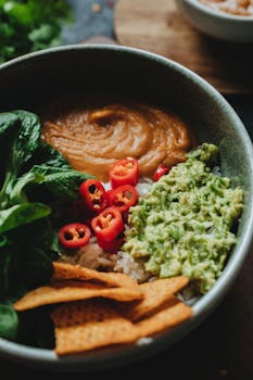 A vibrant vegan bowl featuring avocado, rice, chili peppers, and leafy greens, perfect for a healthy meal.