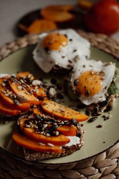 Close-up of gourmet bruschetta topped with persimmons, fried eggs, and seeds on a plate.