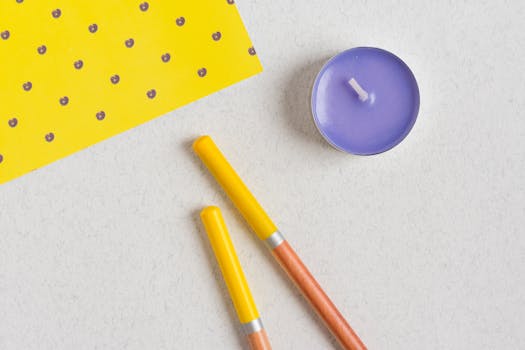 Bright and colorful flat lay featuring a candle, pens, and patterned paper on a white background.