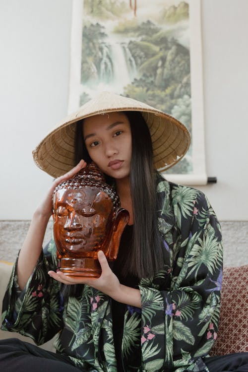 Woman wearing a Conical Hat holding a Wooden Buddha Head 