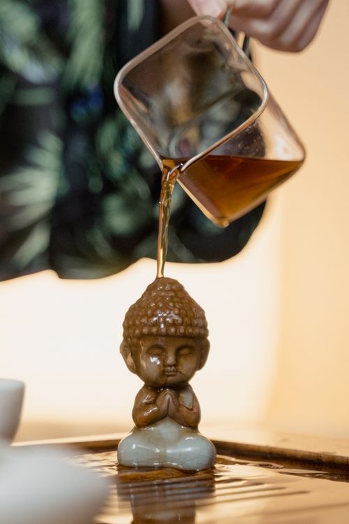 Free Close-up of tea being poured over a small ceramic Buddha statue during a traditional tea ceremony. Stock Photo