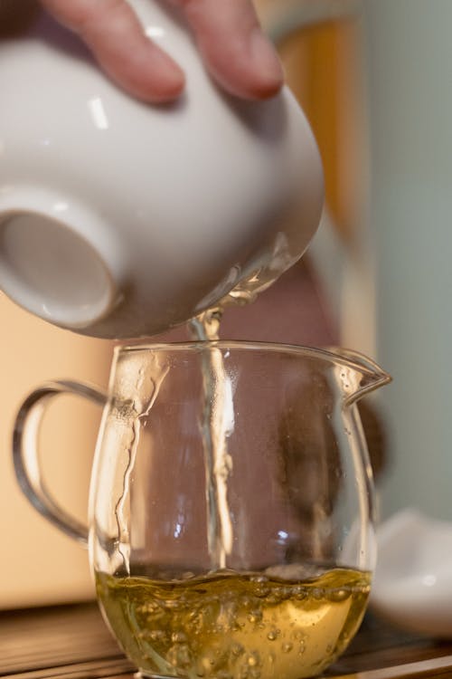 Person Pouring Tea Into a Glass Tea Pot