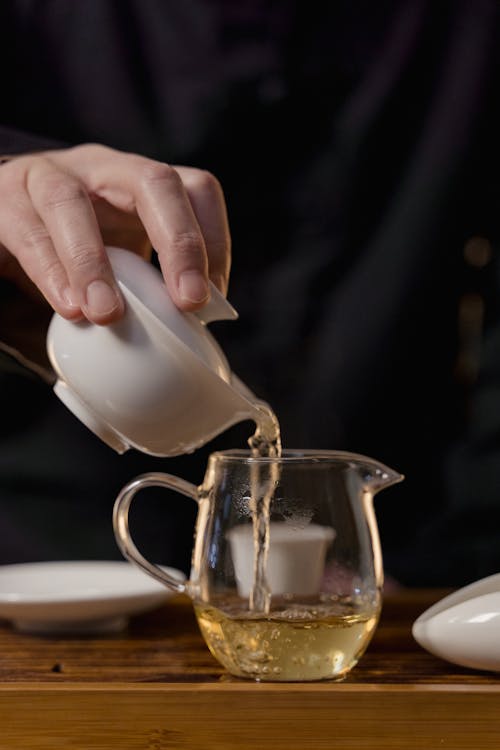 Hand Holding Ceramic Gaiwan and Pouring Tea in Glass Teapot