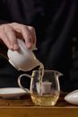 Hand Holding Ceramic Gaiwan and Pouring Tea in Glass Teapot