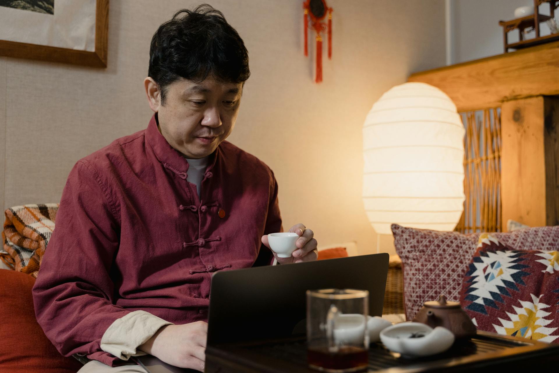 A Man Holding a Teacup While Using His Laptop