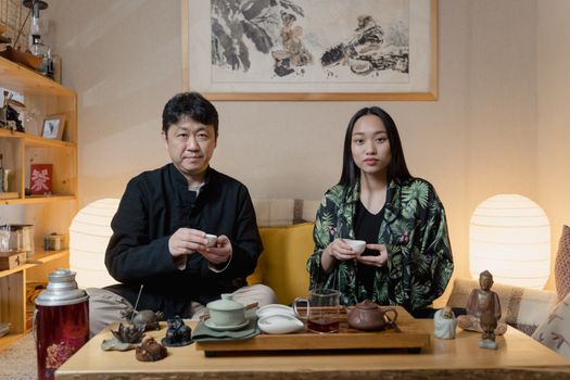 Two people performing a traditional Asian tea ceremony in a cozy indoor setting.