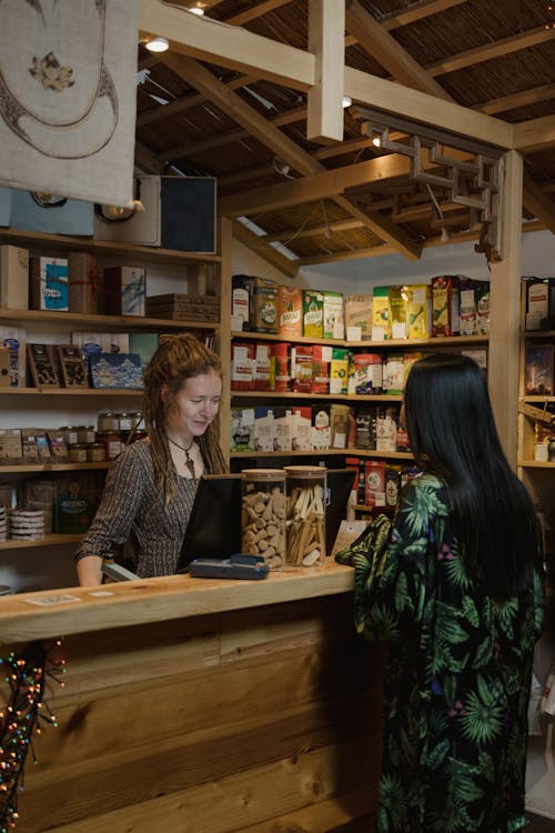 Woman in Tropical Print Dress Ordering in Front of Cashier Behind the Counter