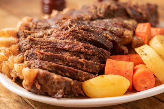 Platter of sliced tender pot roast beef with chunky carrots, potatoes and soft roasted onions
