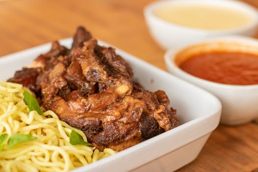 Delicious braised beef served with noodles and tomato sauce, showcasing food photography at its best.