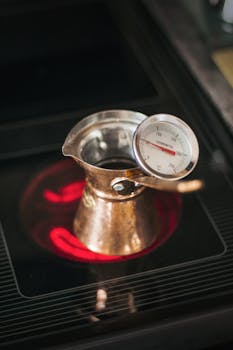 A copper pot with thermometer prepares coffee on a hot stove. Home brewing concept.