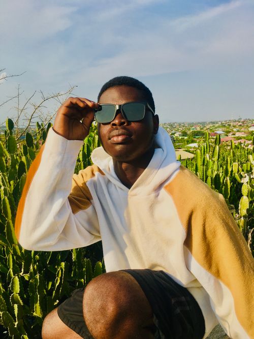 Free Young man wearing sunglasses and hoodie posing outdoors with cacti in the background, Central Ghana. Stock Photo