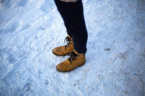 Free Person in Black Pants and Brown Leather Shoes Standing on Snow Covered Ground Stock Photo