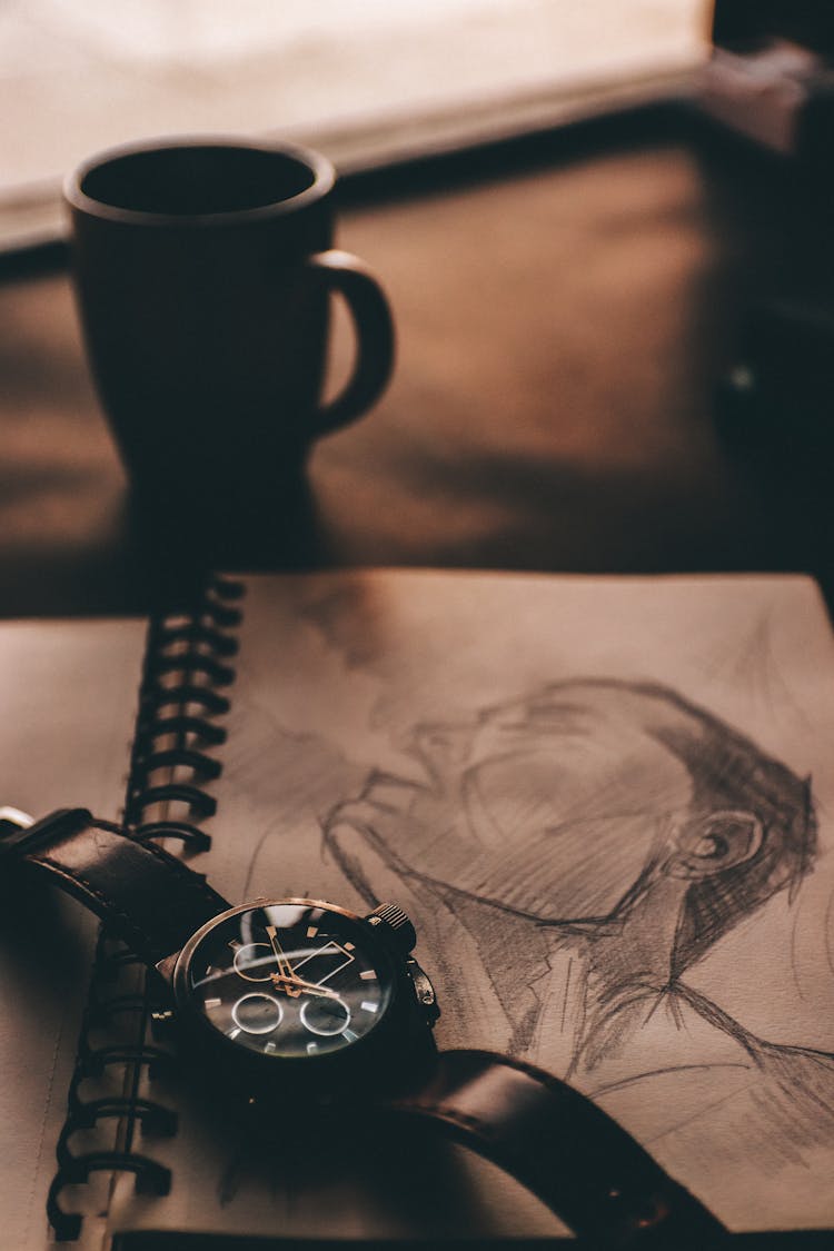 Table With Wristwatch On Sketchbook With Drawing Near Coffee Cup