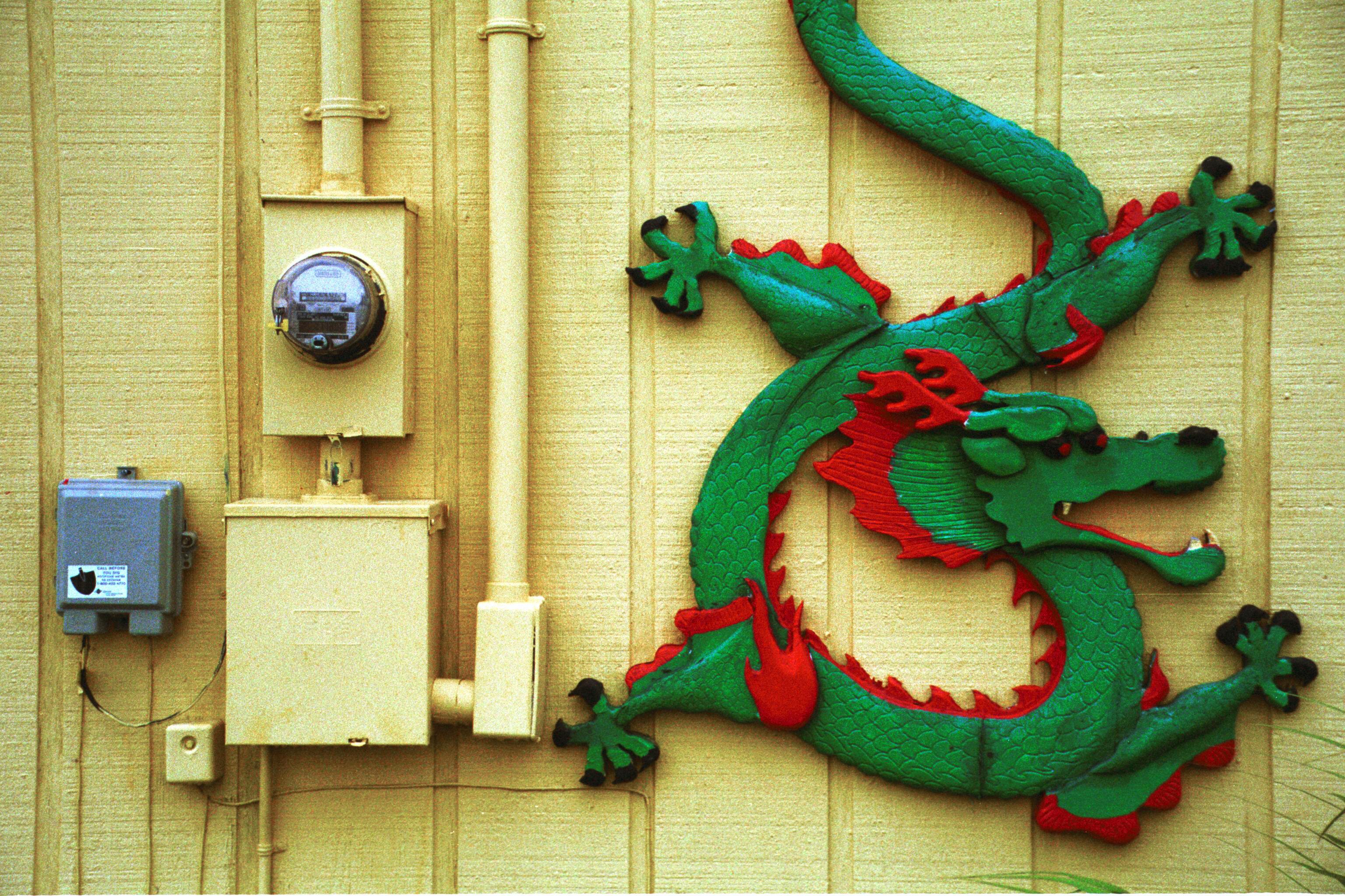 Vibrant dragon wall decor on a yellow wall beside electrical meters.