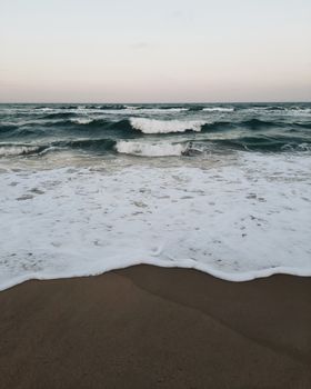 Captivating view of gentle ocean waves hitting a sandy beach during sunset, creating a peaceful ambiance.