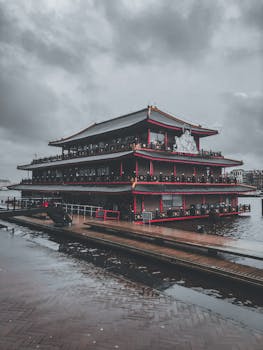 A large traditional pagoda reflects in rain-soaked streets of Amsterdam under stormy skies.