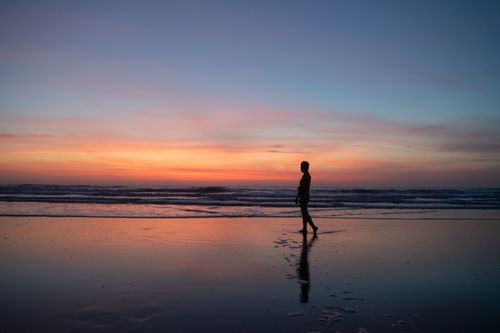 Free Full body side view of anonymous person strolling on wet coast near rippling sea at sundown time during summer vacation Stock Photo