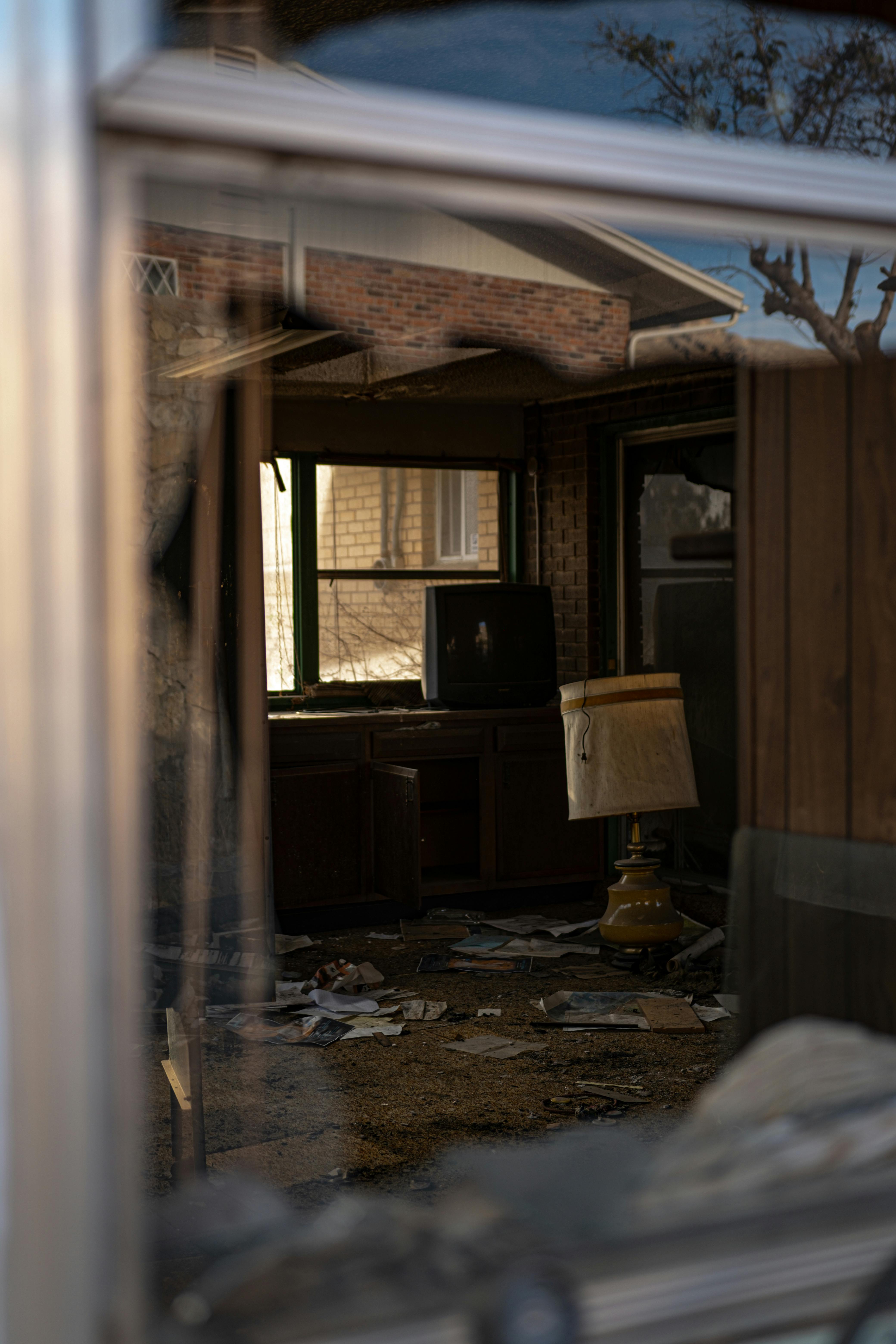 View through a glass window of an abandoned house interior with old furniture and debris.