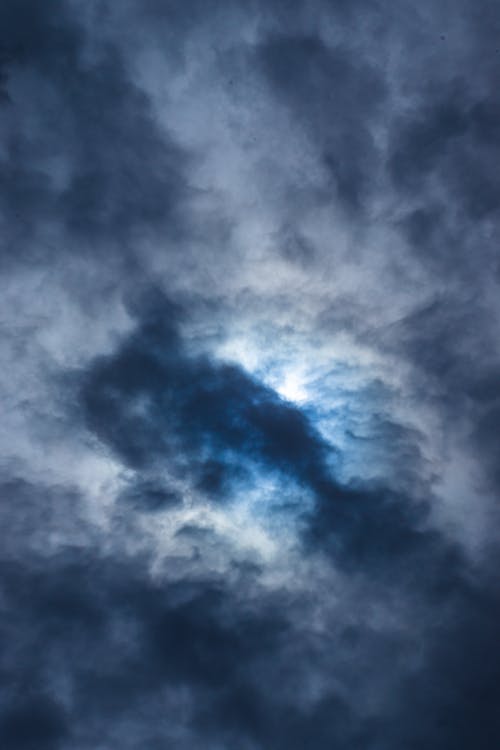 From below of fluffy dense gray cumulus clouds floating high in air on gloomy sky in nature in overcast weather