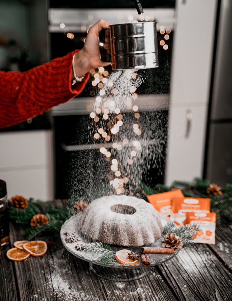 


A Person Dusting Powdered Sugar On A Cake