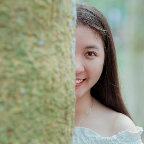 Free Happy young woman peeking from behind a tree, outdoors in nature. Stock Photo