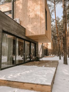 Wooden house with large glass windows on snowy day in forest setting, perfect for winter retreats.