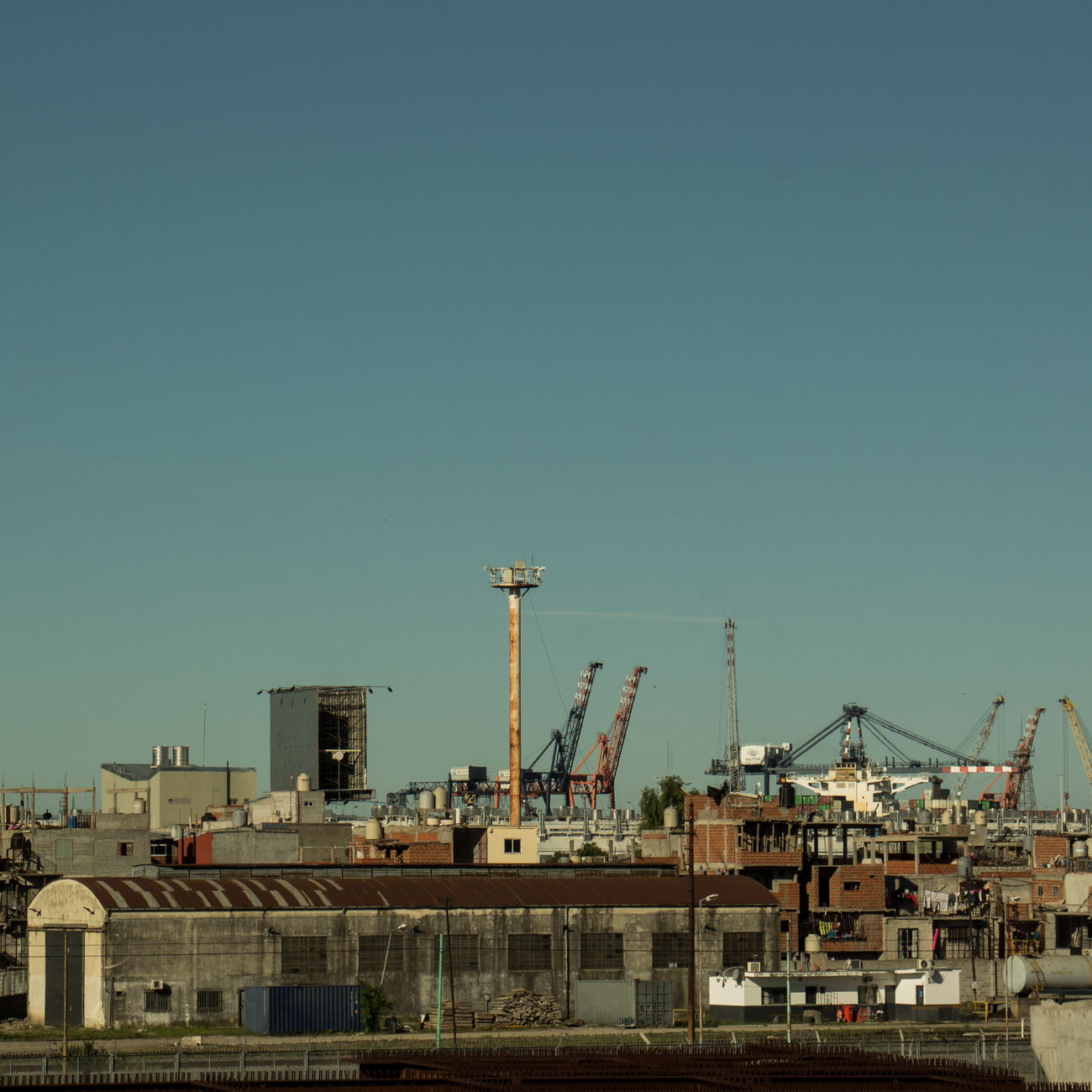 View of an industrial area with tower cranes in Buenos Aires, Argentina, under a clear blue sky.