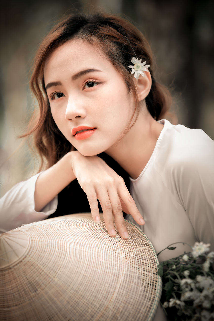 Portrait of a Vietnamese woman in a white ao dai, holding a conical hat, with a serene expression.