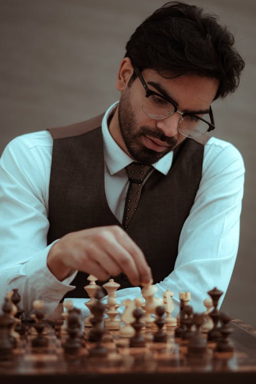 Focused bearded male in classy suit and eyeglasses playing chess game in studio