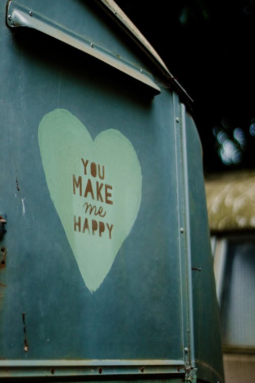 You Make Me Happy inscription written on aged metal mailbox with painted heart placed in street in city on blurred background