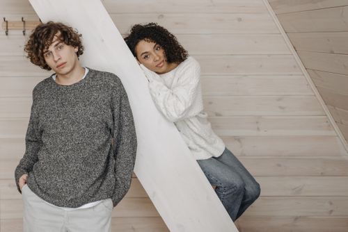 Free Young diverse couple posing casually indoors in warm sweaters, exuding a relaxed and cozy atmosphere. Stock Photo