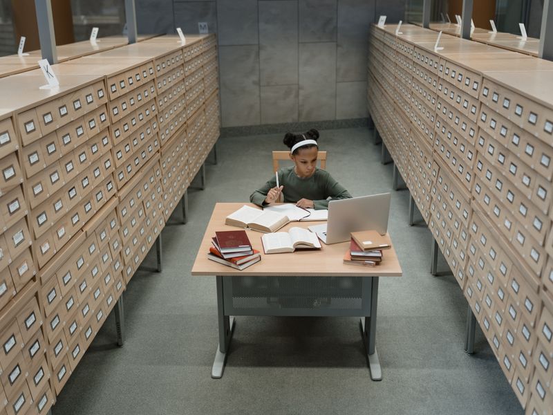 Student studying with laptop and books in a historical library archive room, surrounded by card catalog drawers - history day project sites
