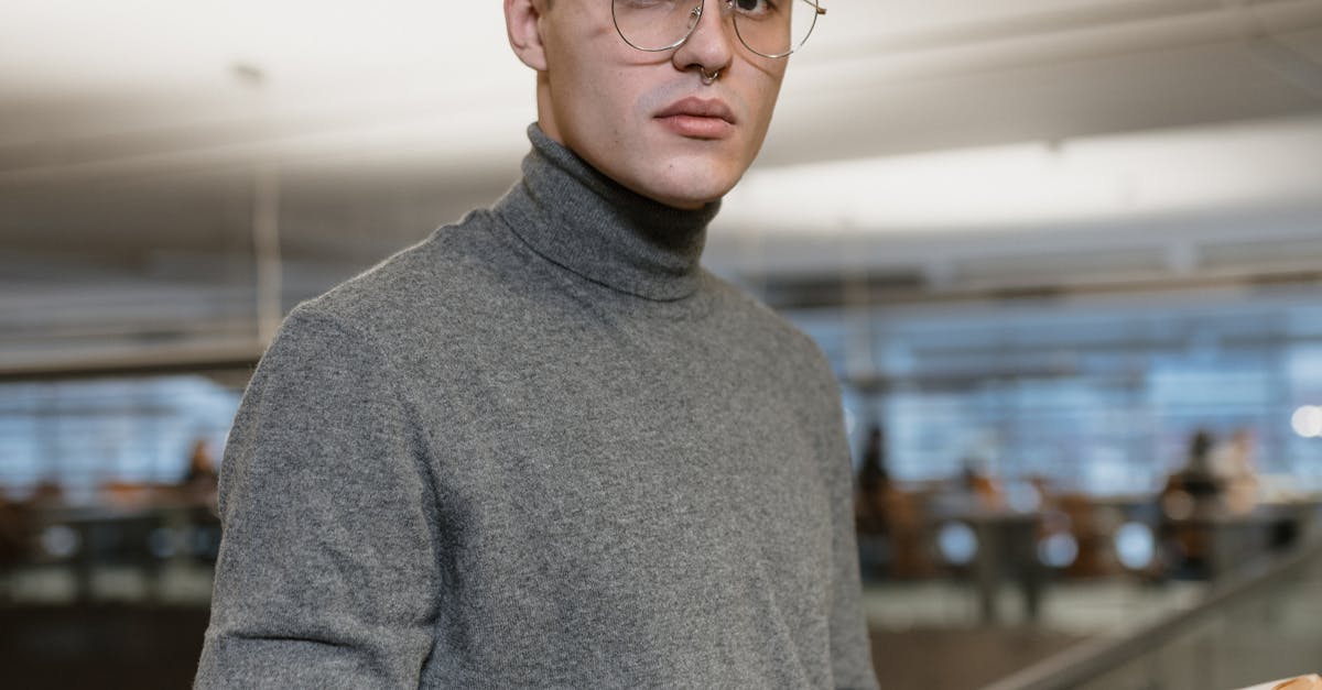Portrait of a young man in a library holding a book and wearing glasses, exuding intellectual vibes.