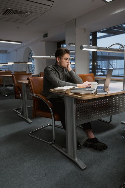 Young man using a laptop in a contemporary library environment, focused on studying. Young man using a laptop in a contemporary library environment, focused on studying.