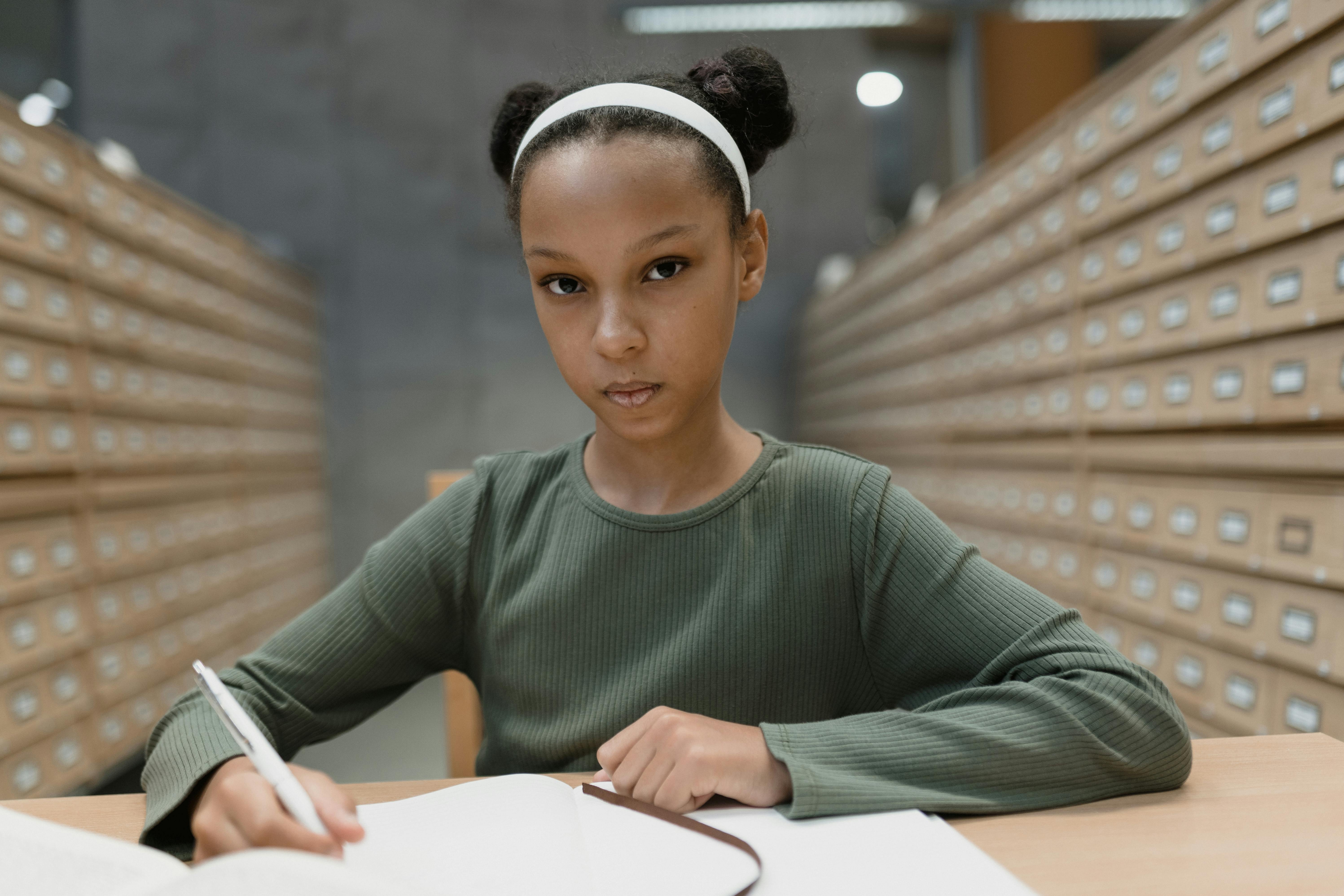 a woman with hair bun writing on a notebook while looking at the camera