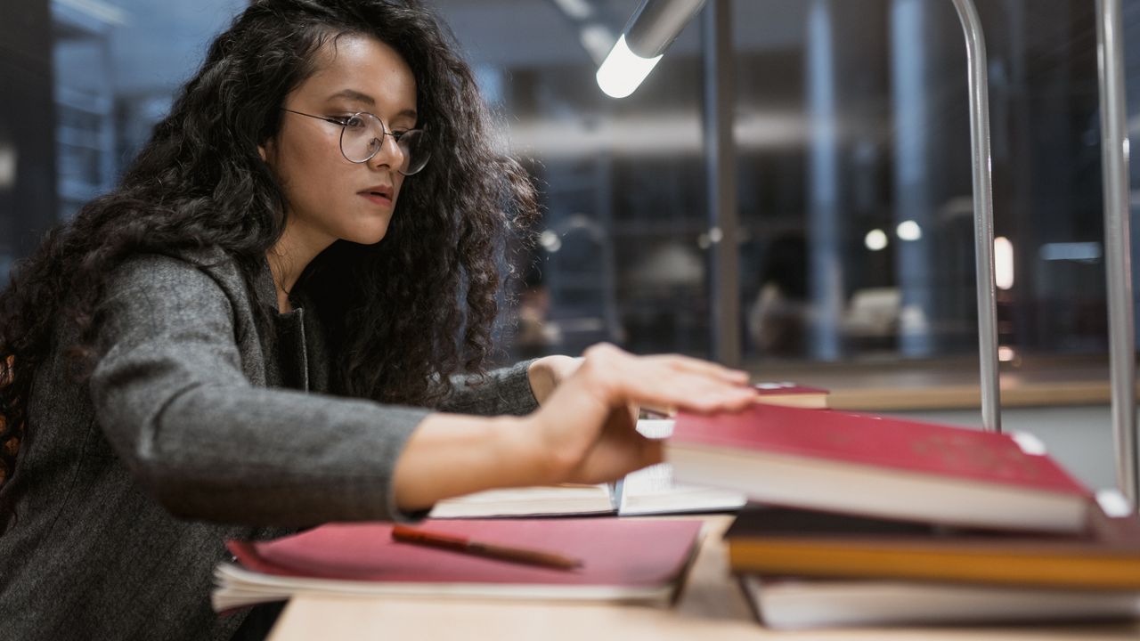 A student studying at a desk under a lamp in a library.