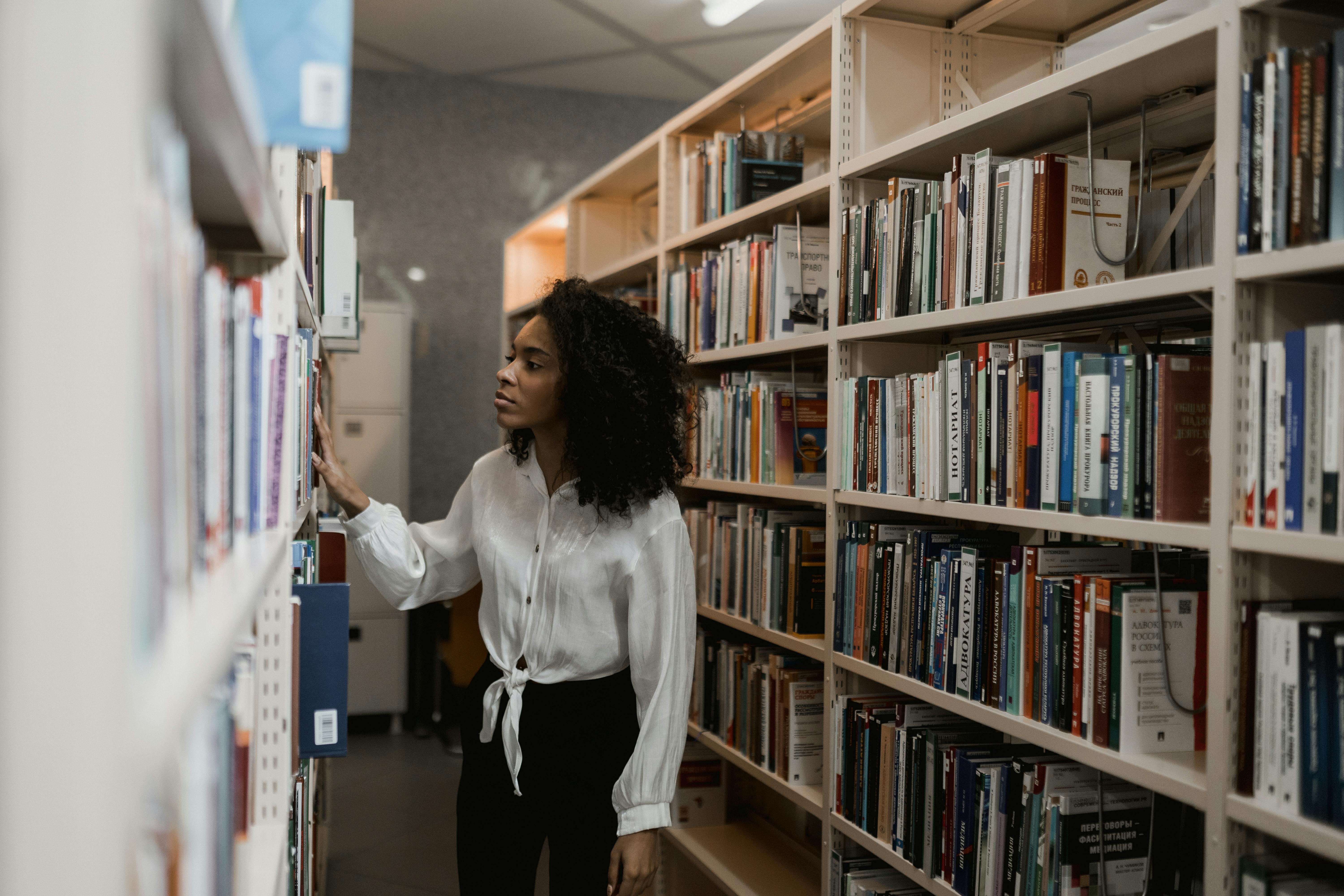 woman in white long sleeve searching at book shelves