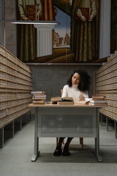 A woman engrossed in reading at a desk surrounded by library card catalogs.