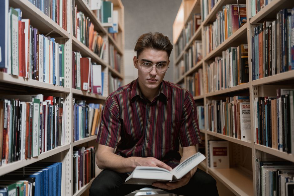 Focused young man reading a book amid library bookshelves. Perfect for educational content. Focused young man reading a book amid library bookshelves. Perfect for educational content.