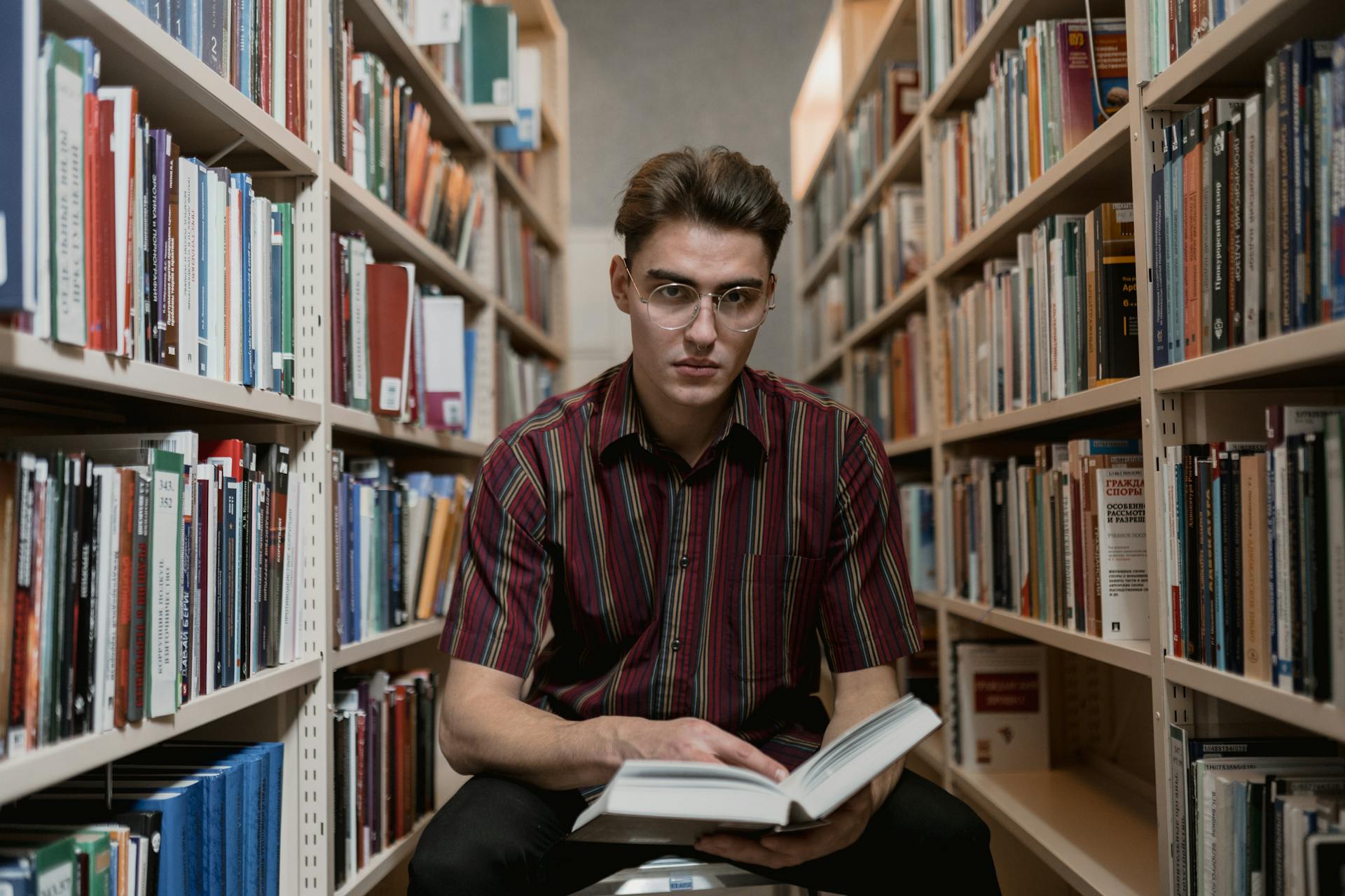 Focused young man reading a book amid library bookshelves. Perfect for educational content.