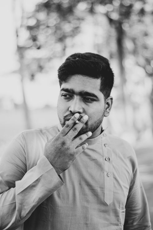 Free A contemplative man in black and white holding a cigarette outdoors. Stock Photo