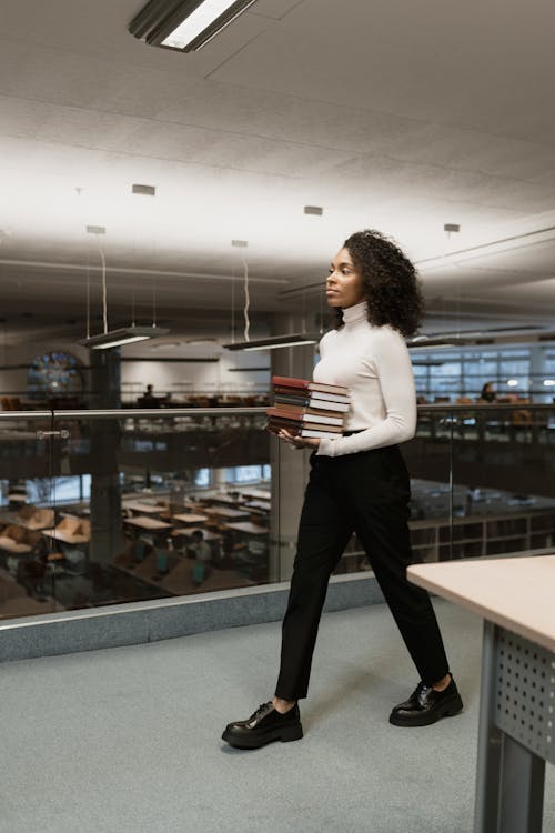 Woman in White Turtleneck Top Holding a Stack of Books