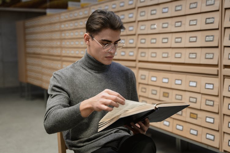 A Young Man Reading A Book In A Library