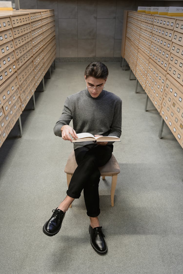 A Young Man Reading A Book In A Library