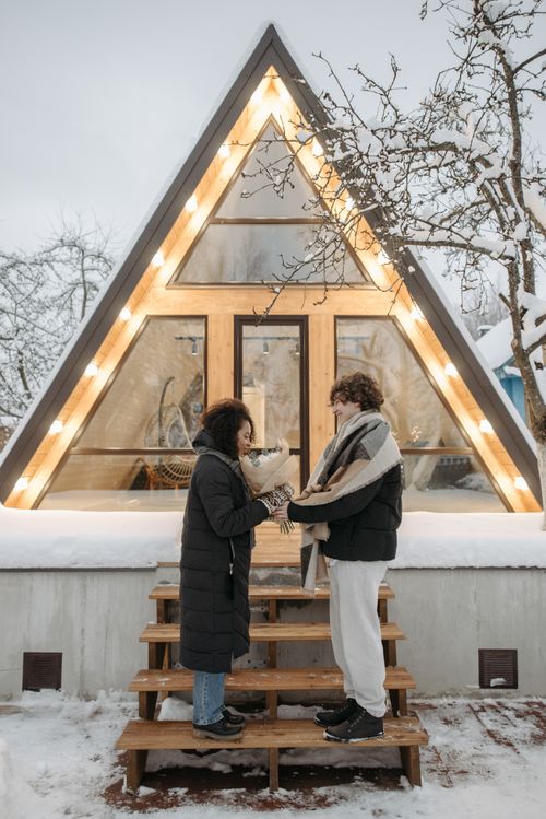 Free Couple shares a sweet winter moment in front of a lit A-frame cabin. Stock Photo