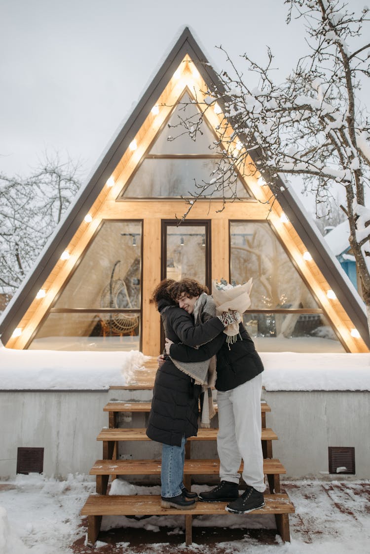 A Couple Hugging Each Other While Standing On Concrete Steps Near A Cabin