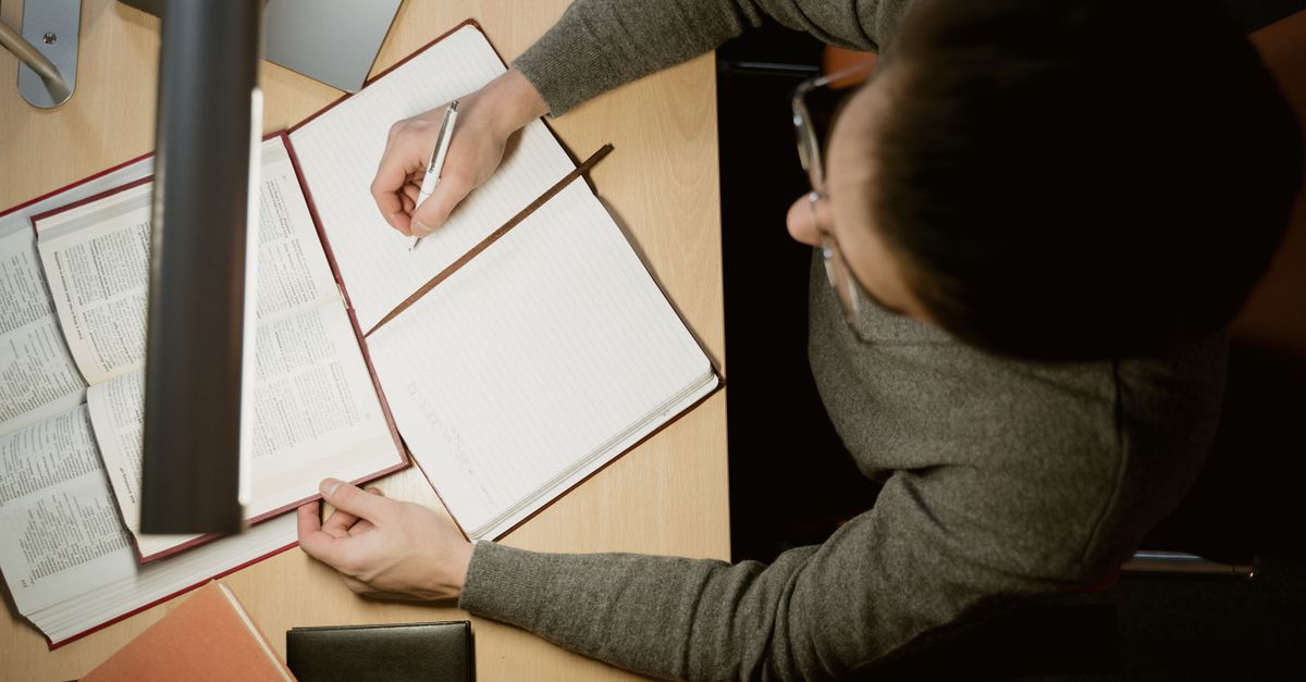 Top View Shot of a Man Writing on a Notebook · Free Stock Photo