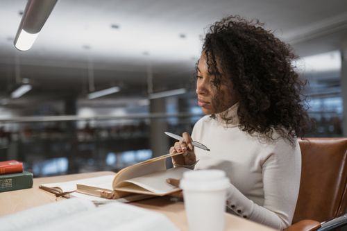 Free A woman with curly hair studying intently at a library desk with books and coffee. Stock Photo