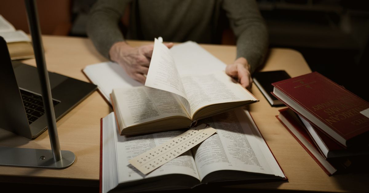 A person engrossed in studying with open books on a desk.