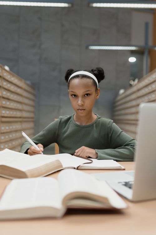 Free Focused young girl studying in a library with books and notebook. Stock Photo